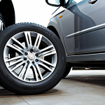 A professional driving instructor demonstrating vehicle maintenance checks (tire pressure, oil levels) on a modern car in a clean, well-lit garage. Fully clothed in work attire, appropriate content, safe for work, perfect anatomy, natural proportions, professional.